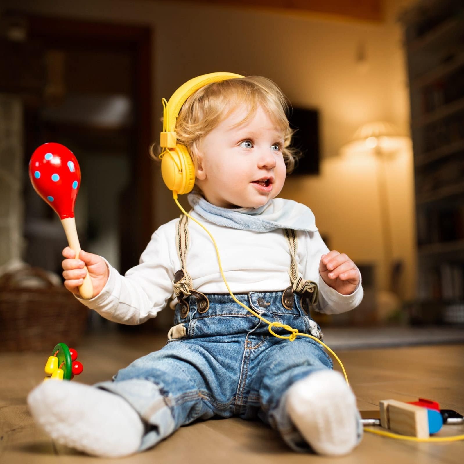 Little boy with earphones, listening music and plying musical in Cute little boy at home sitting on wooden floor wearing earphones, listening music from smart phone and plying musical instrument.