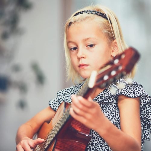 Little girl learning to play to the guitar at the home.