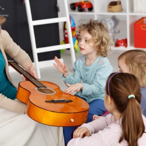 Young teacher having music lesson with small kids in kindergarten